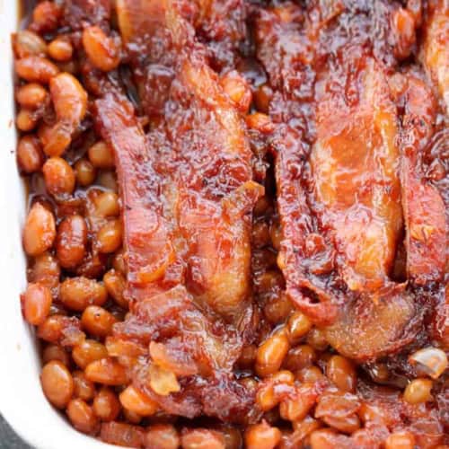 Boston baked beans topped with strips of cooked bacon in a white rectangular dish—a classic comfort food perfect as a hearty side dish.