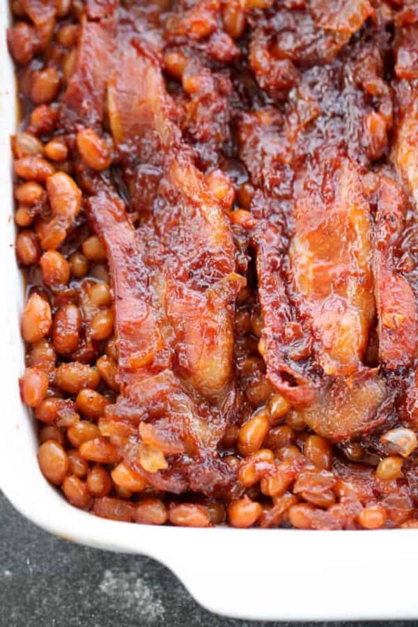 Boston baked beans topped with strips of cooked bacon in a white rectangular dish—a classic comfort food perfect as a hearty side dish.