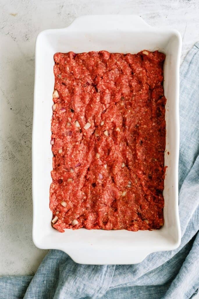 Beef mixture pressed into the bottom of a baking dish.