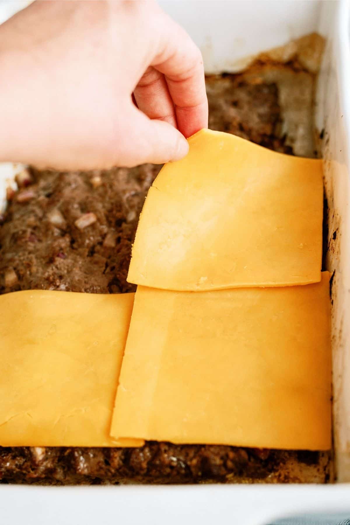 Placing cheese slices on top of cooked hamburger 