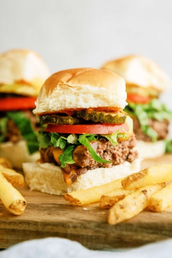 Baked Cheeseburger Sliders on top of a cutting board surrounded by french fries.
