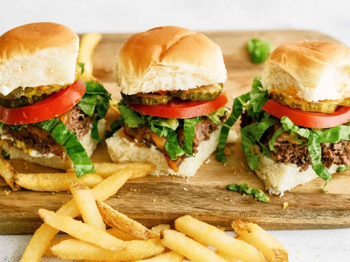 3 Baked Cheeseburger Sliders in a row on a cutting board with fries