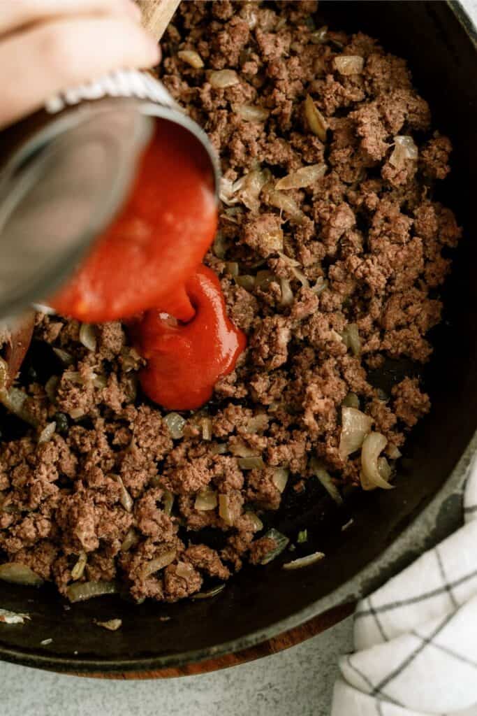 Pouring manwich into a skillet of ground beef.
