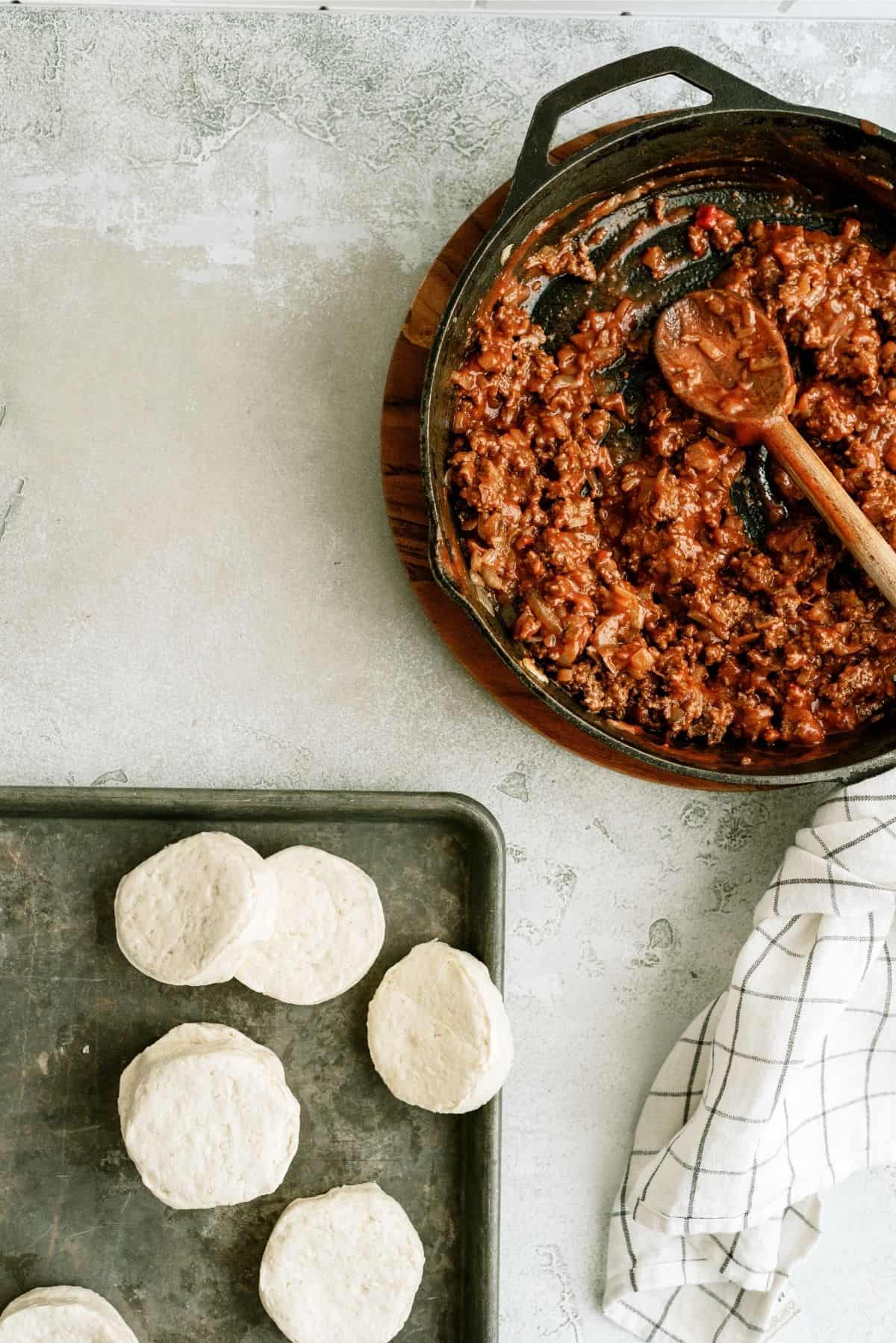 Sloppy Joe mixture in pan and uncooked biscuits on a baking sheet