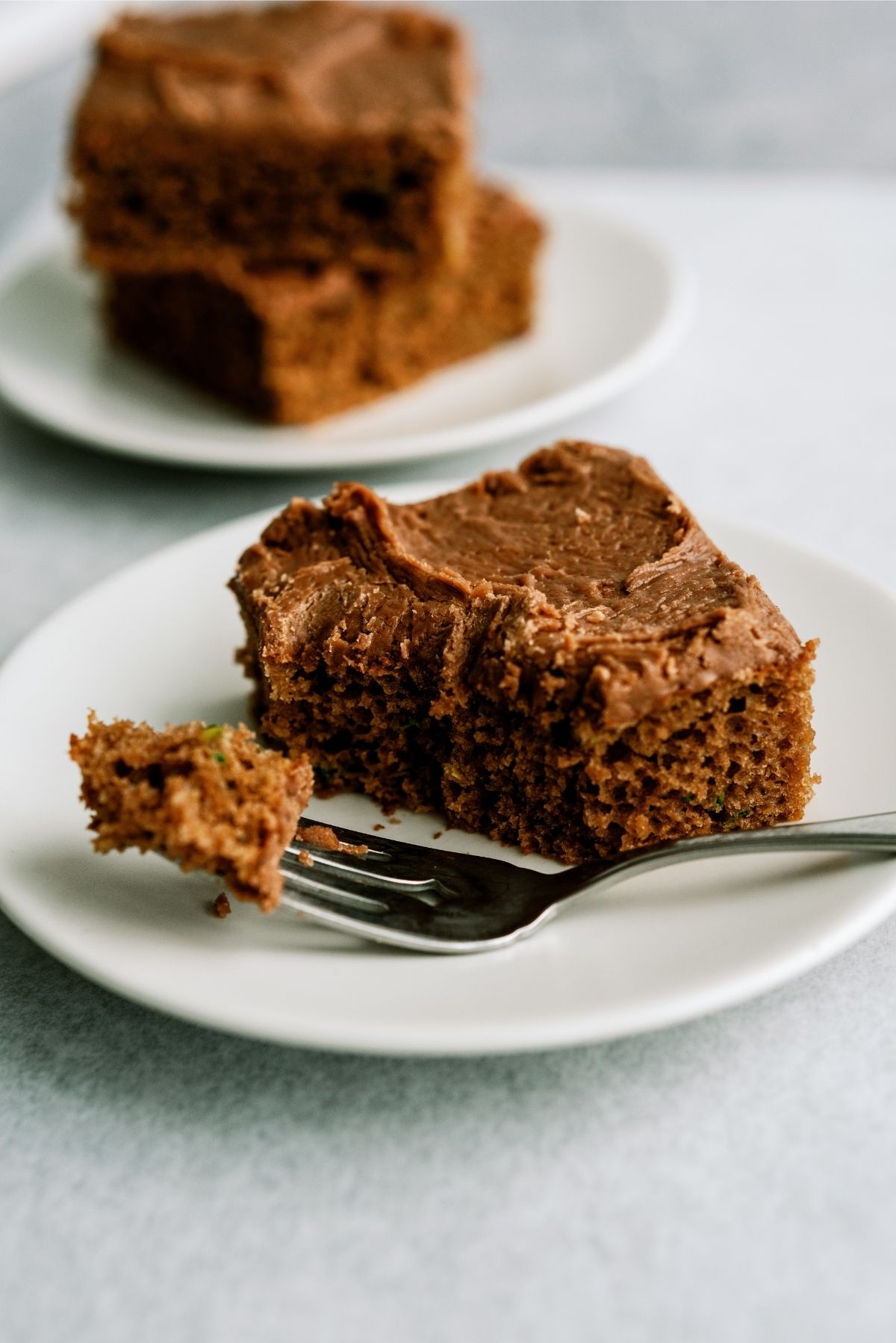 Slice of Chocolate Zucchini Sheet Cake on a white plate with a fork