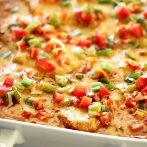 A casserole dish filled with a baked cheesy casserole topped with chopped red and green bell peppers and diced tomatoes.