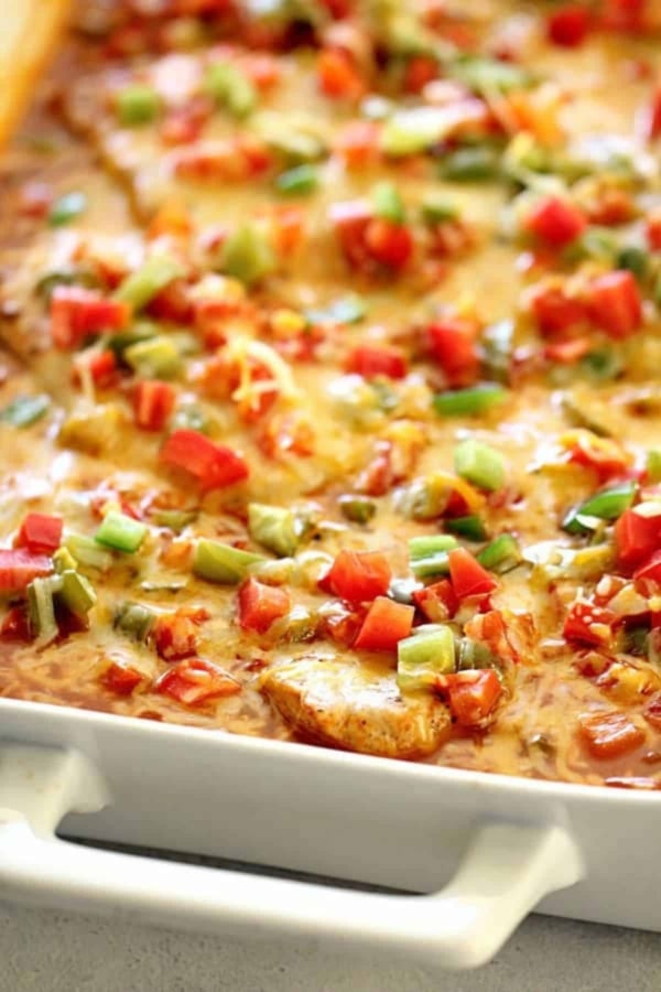 A casserole dish filled with a baked cheesy casserole topped with chopped red and green bell peppers and diced tomatoes.