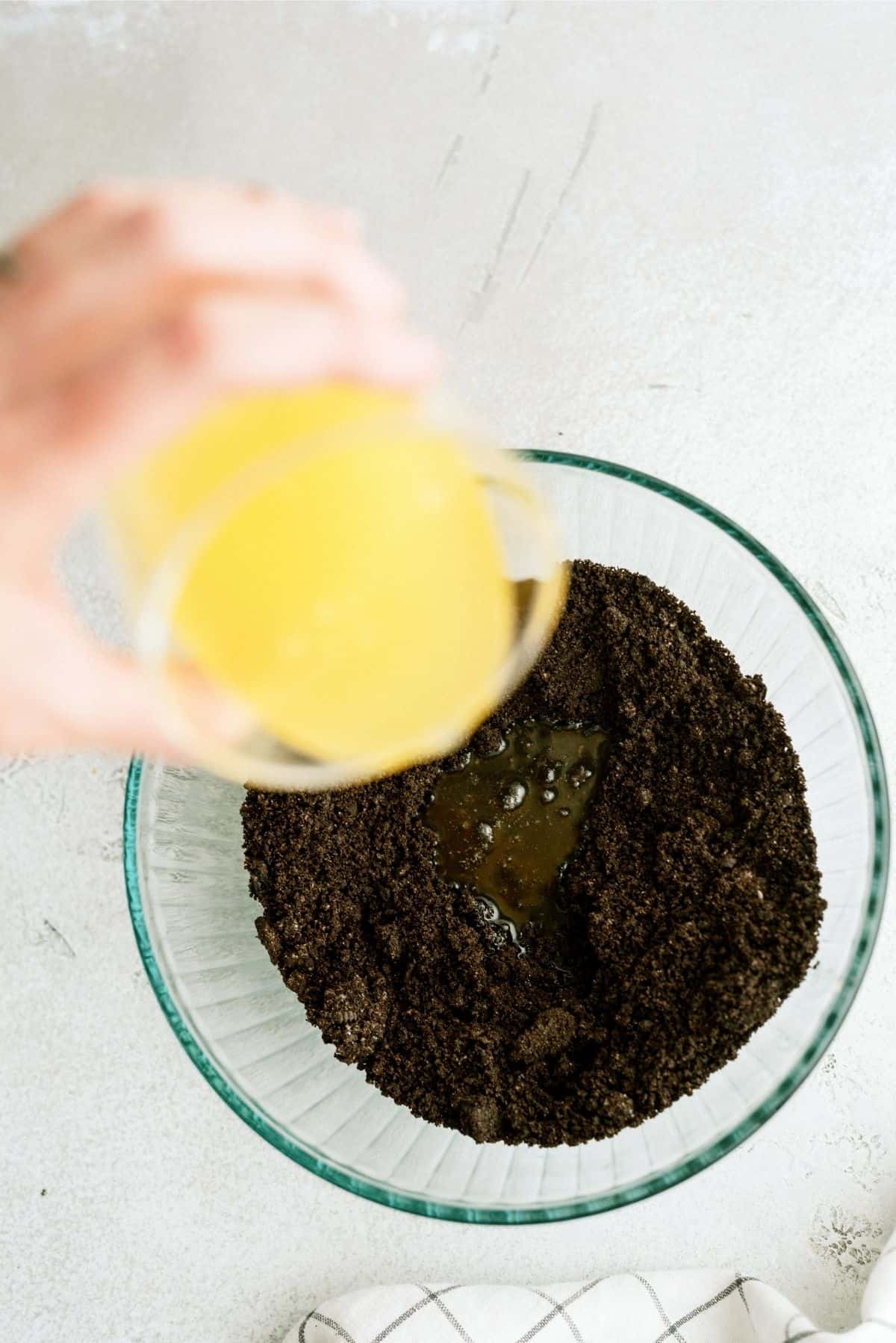 Pouring melted butter into a bowl of crushed oreos