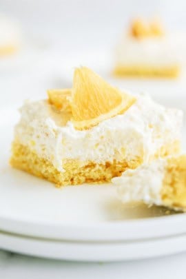 A slice of Pineapple Orange Cake on a plate with a section of the slice cut off.