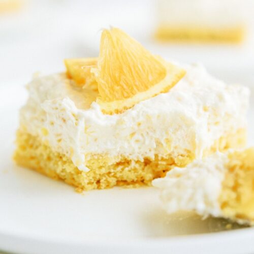 A slice of Pineapple Orange Cake on a plate with a section of the slice cut off.