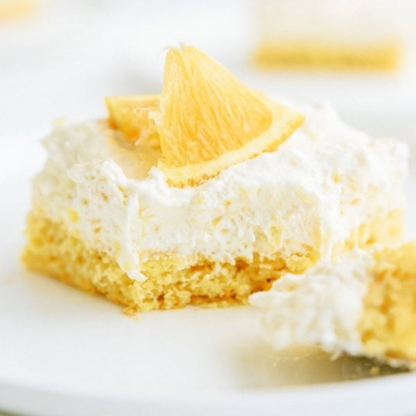 A slice of Pineapple Orange Cake on a plate with a section of the slice cut off.