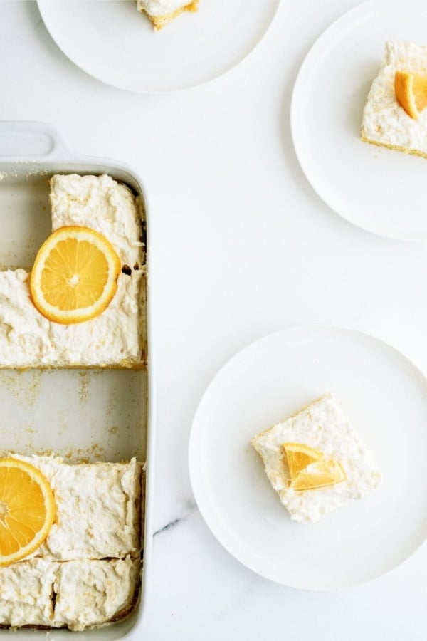 Slices of Pineapple Orange Cake on white dishes with some cake left in the baking dish.