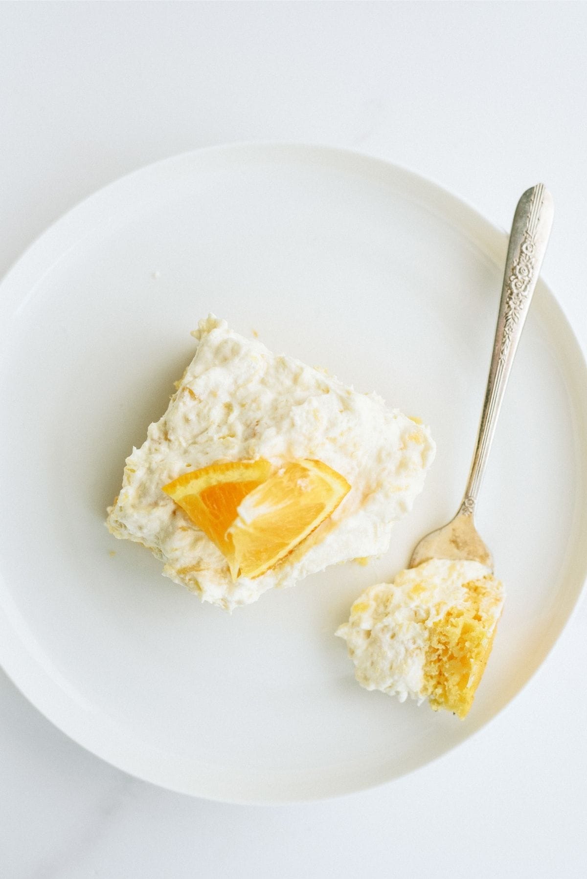 A slice of Pineapple Orange Cake Recipe (Pig Pickin’ Cake) on a white plate with a fork