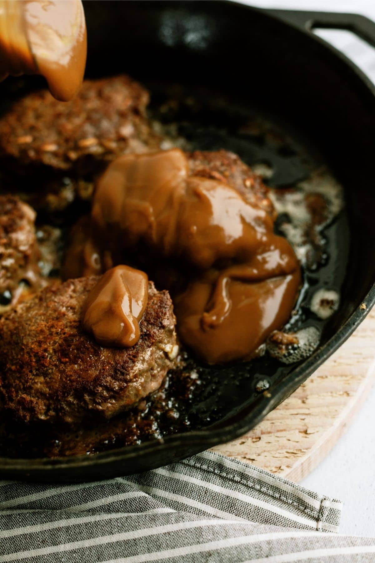 Pouring gravy over cooked Salisbury Steak patties