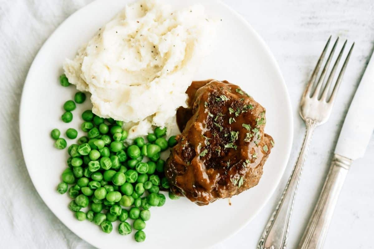 Salisbury Steak on a plate with mashed potatoes with green peas