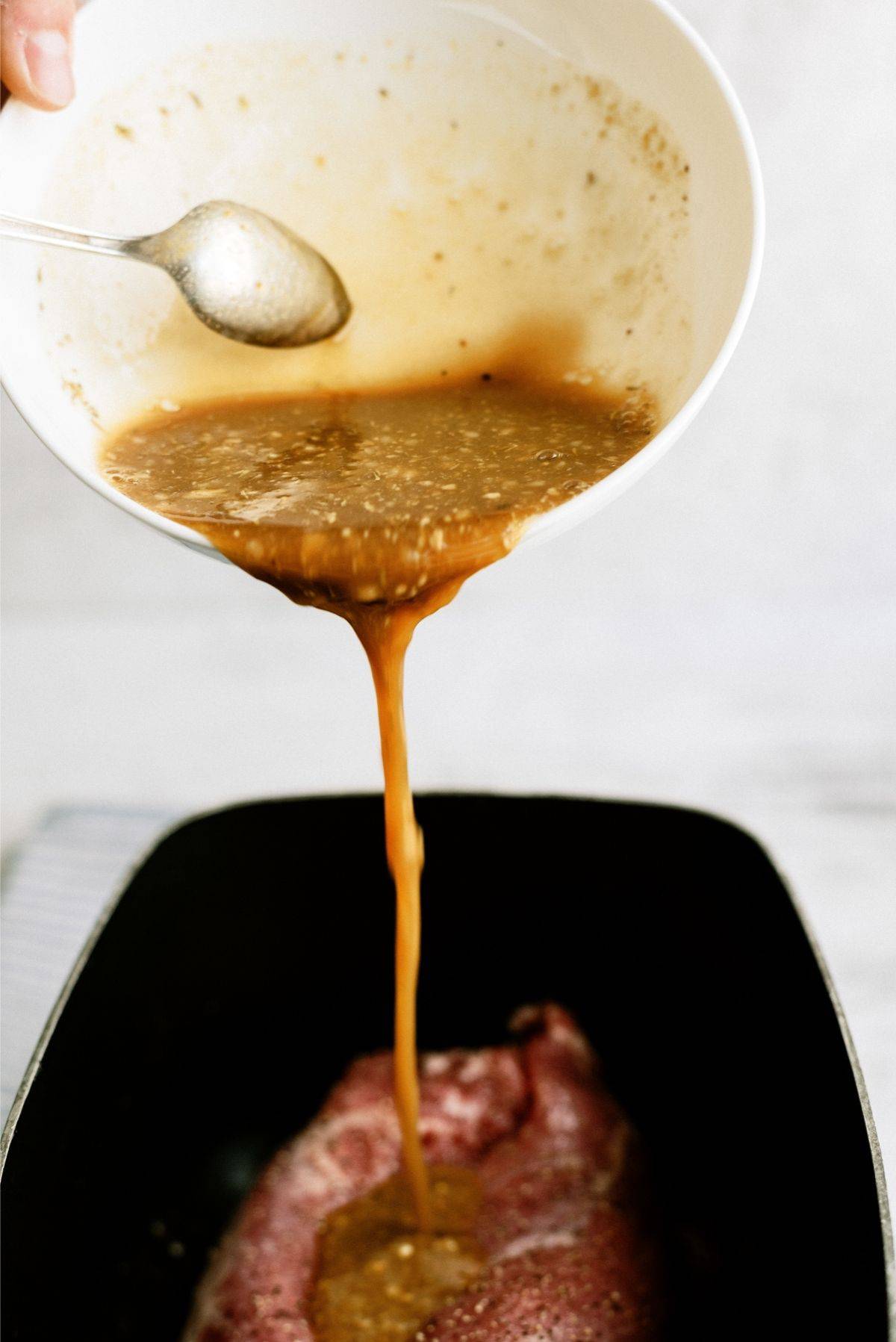 Sauce being poured over uncooked pork loin in slow cooker