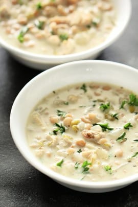Two white bowls filled with creamy chicken and rice soup, garnished with fresh herbs.