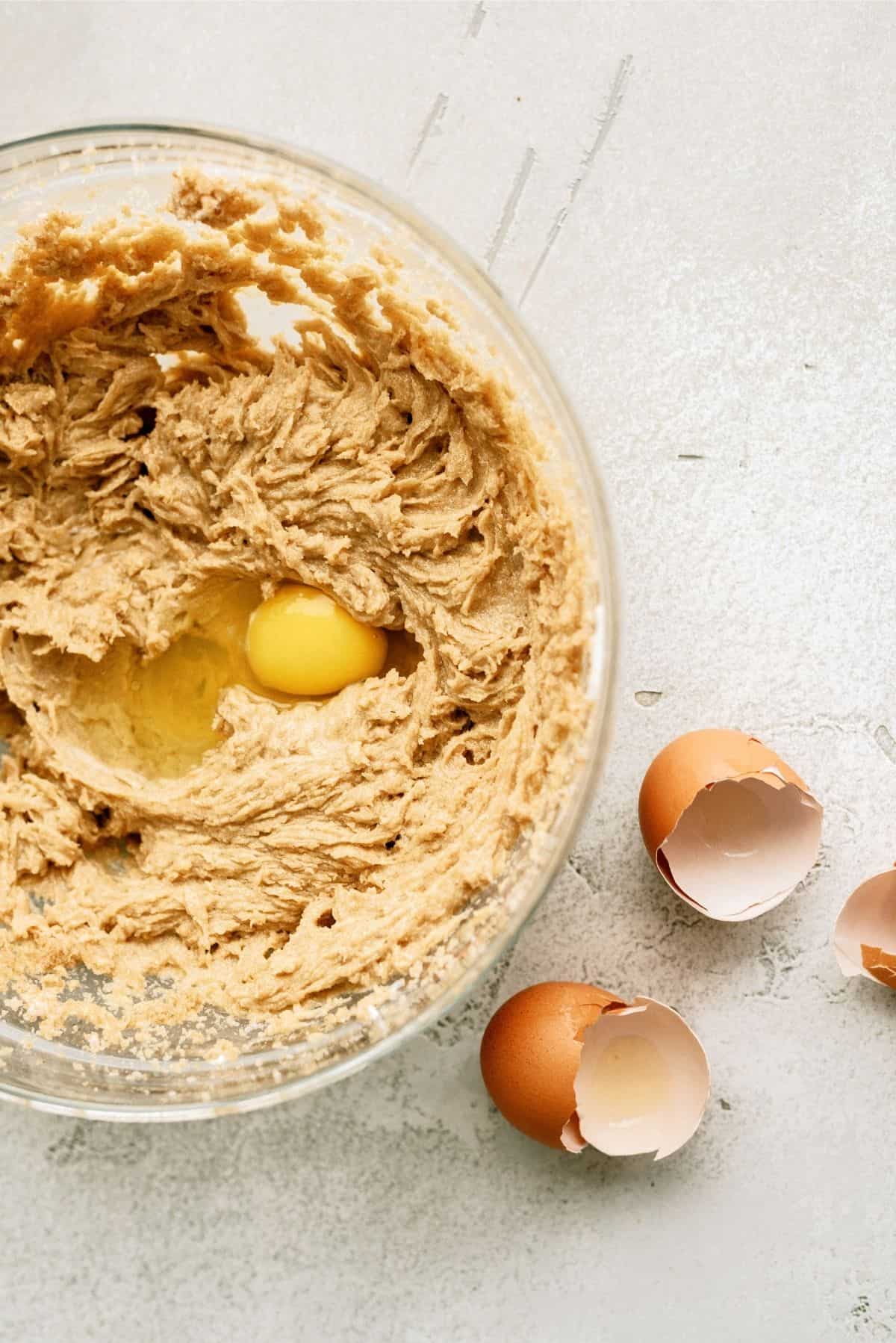 Blondie batter in a glass bowl mixed together with two eggs on top.