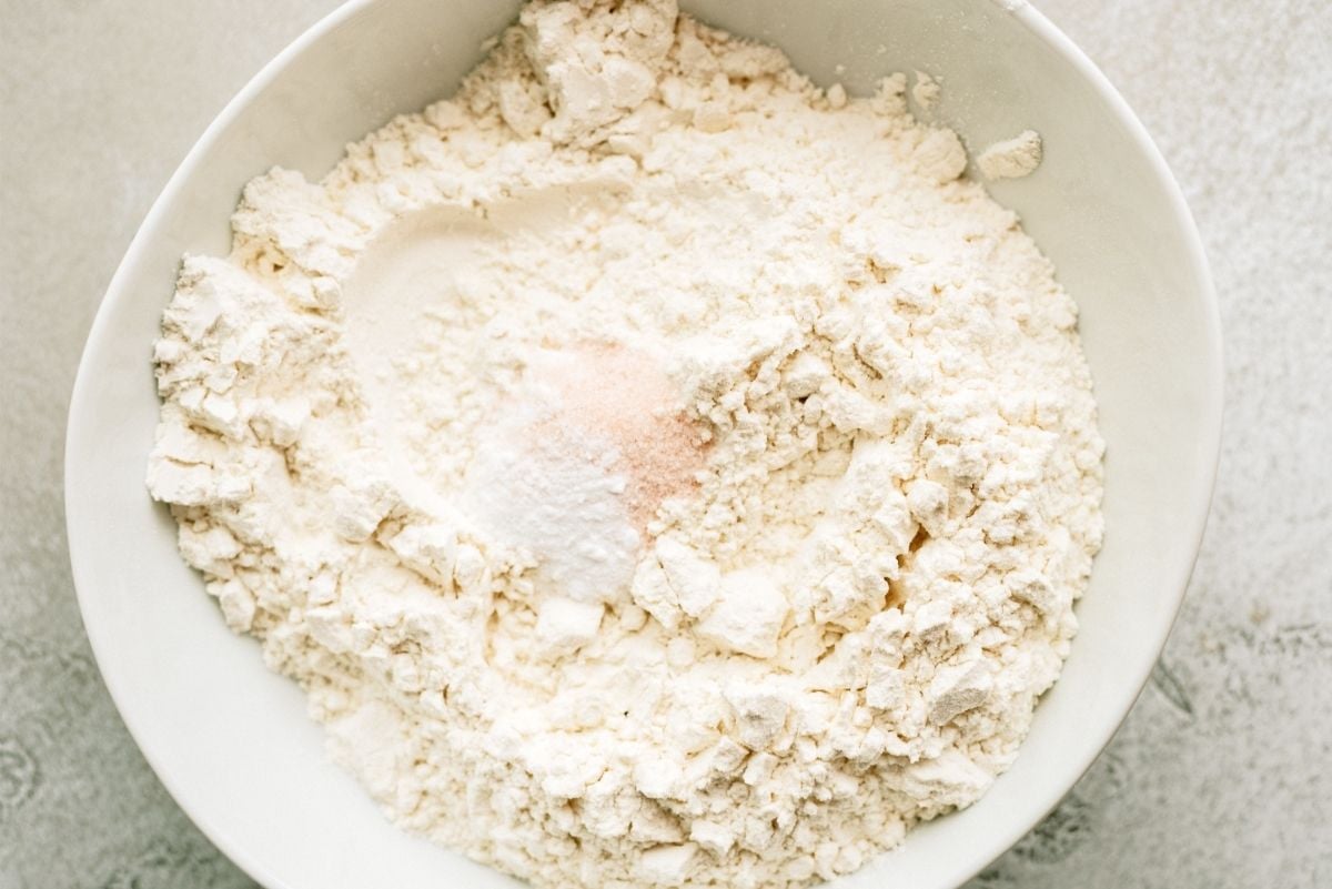Adding dry ingredients to wet dough in a white bowl