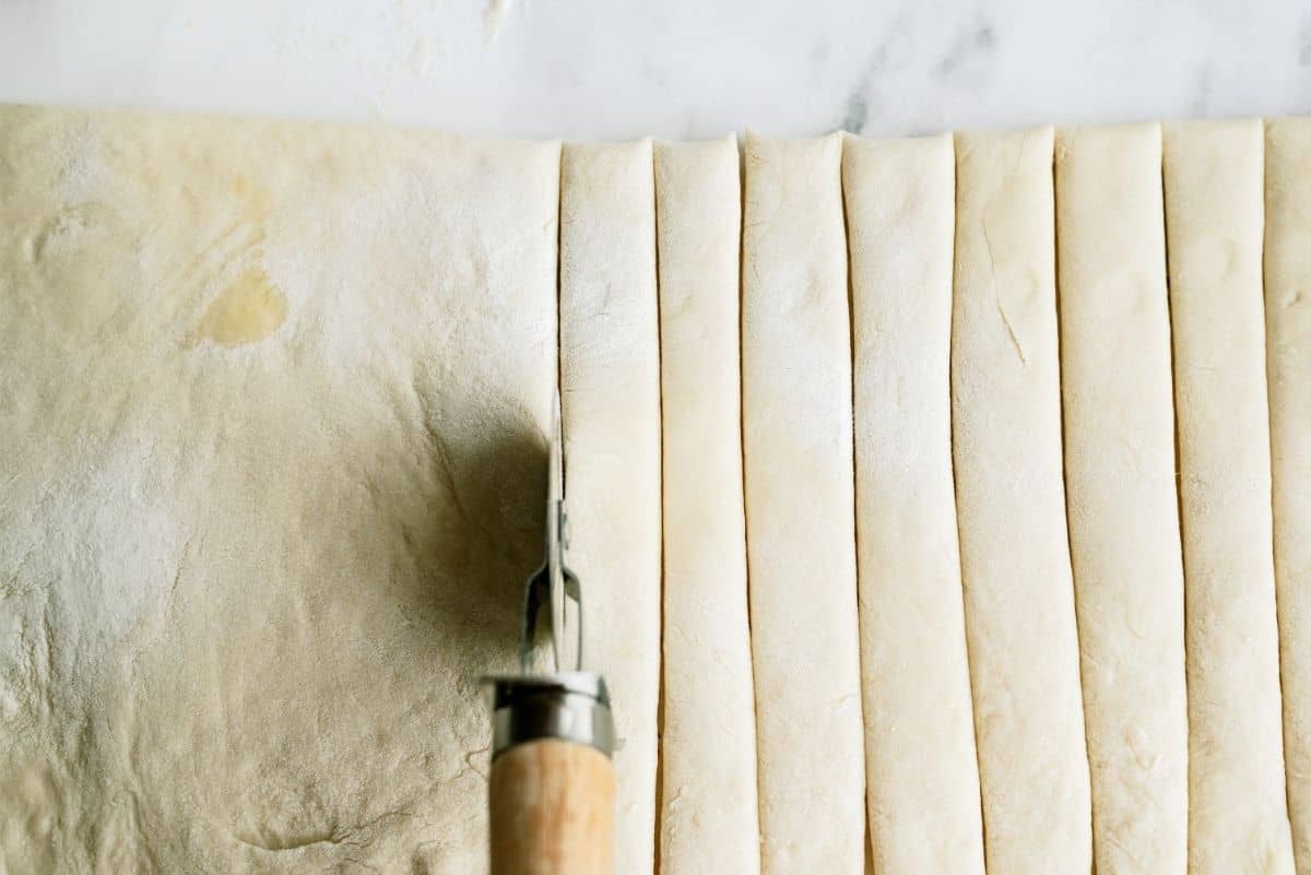 Pizza cutter cutting dough into strips