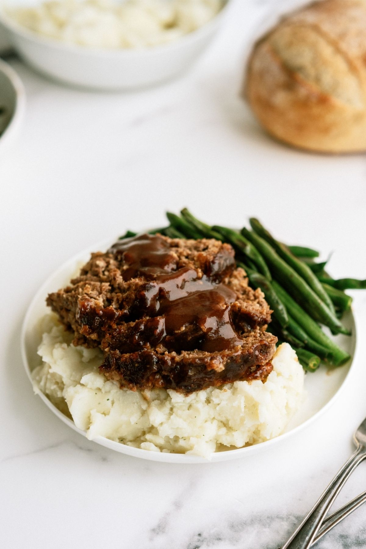 Honey BBQ Meatloaf sliced on a plate with mashed potatoes and green beans