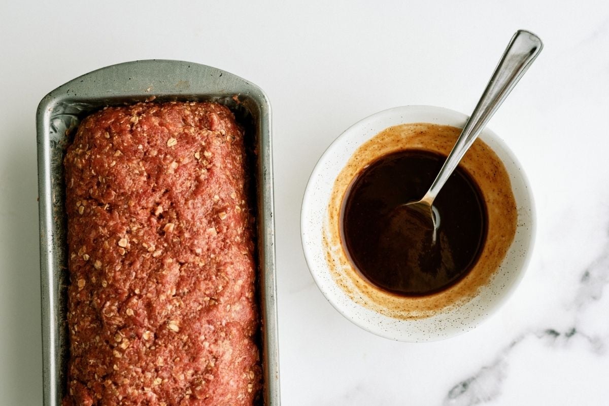 Unbaked meatloaf in loaf pan with a small bowl of Honey BBQ Sauce