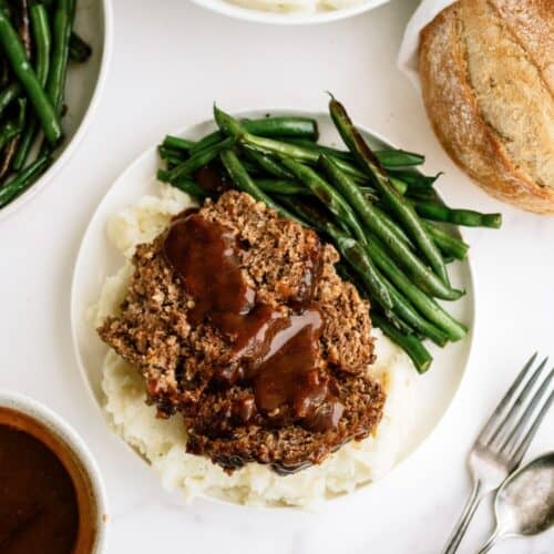 A plate with Honey BBQ Meatloaf served over mashed potatoes with a side of green beans.