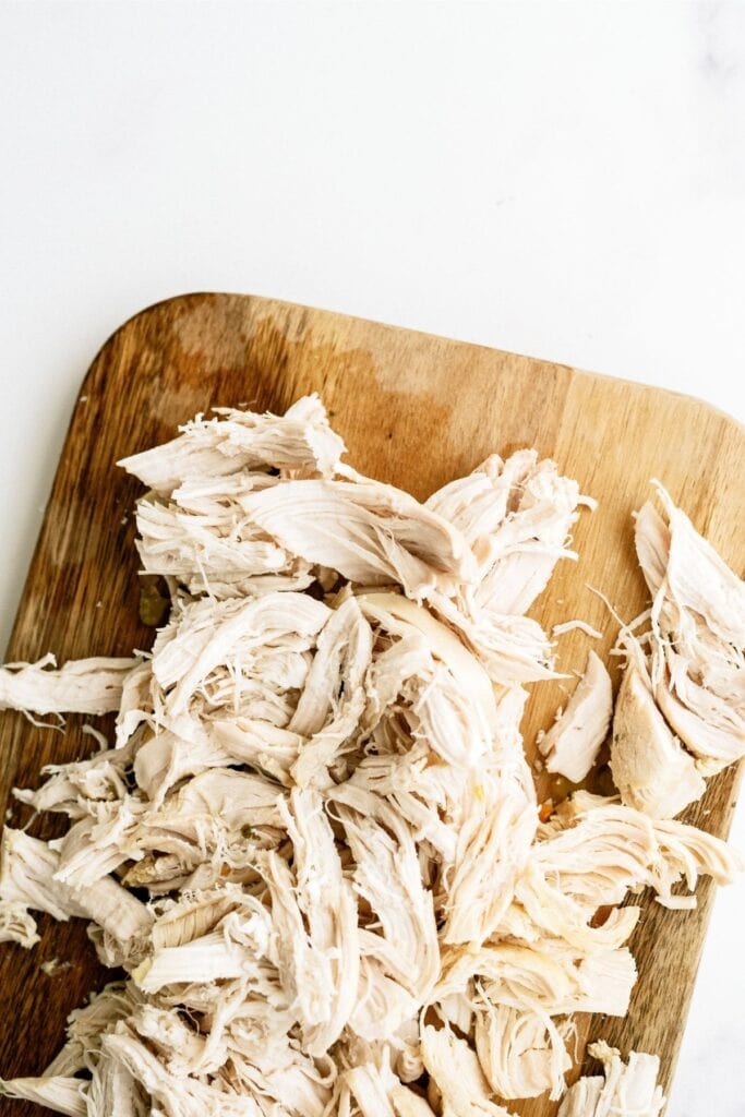 Shredded cooked chicken piled on a wooden cutting board against a white background.