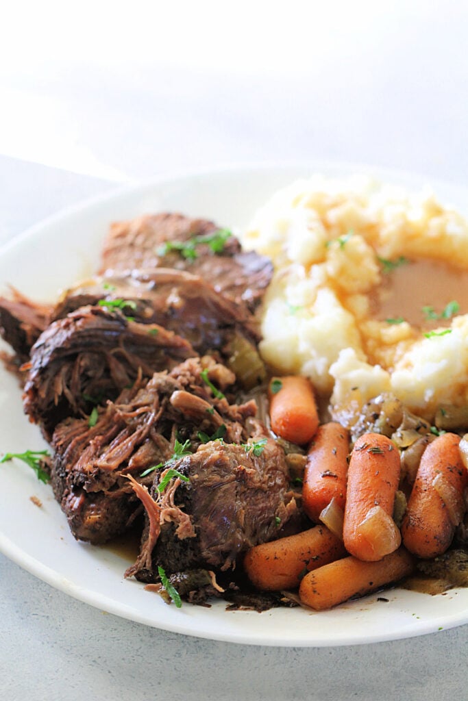 pot roast, mashed potatoes, gravy and cooked carrots on a plate