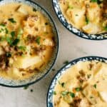 Three bowls of creamy soup containing potatoes, ground meat, and chopped herbs, garnished with fresh parsley.