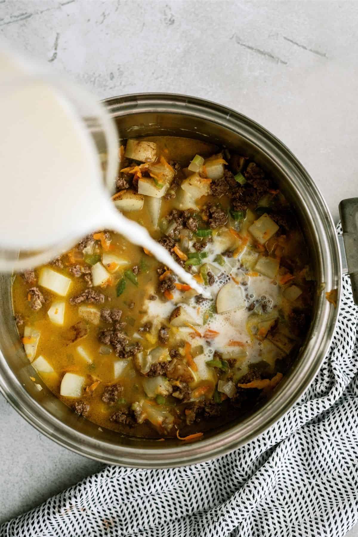 Adding milk to Cheeseburger Soup mixture in saucepan