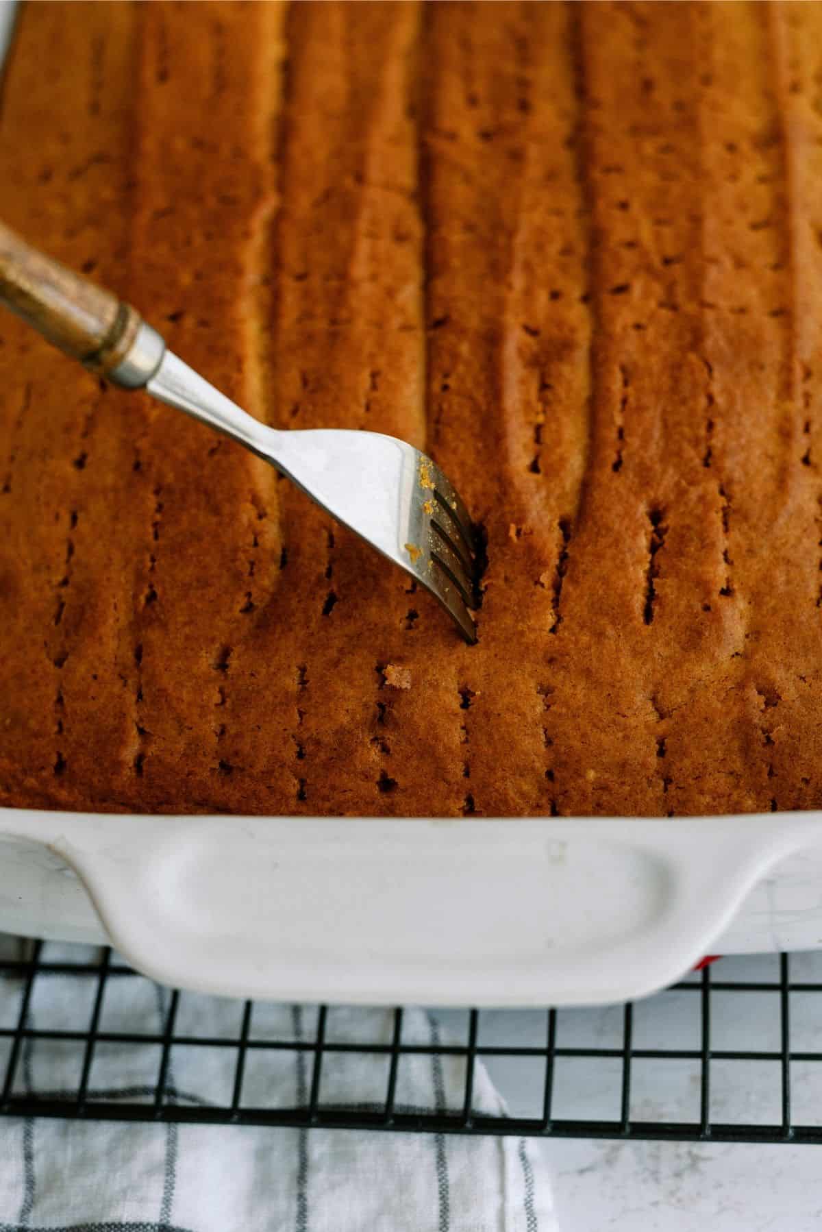 Fork poking holes in baked cake