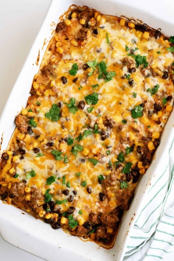 Baked casserole topped with melted cheese, black beans, corn, and fresh cilantro in a white dish.