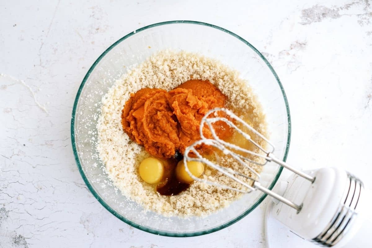 Pumpkin wet ingredients mixed together in glass bowl with hand mixer