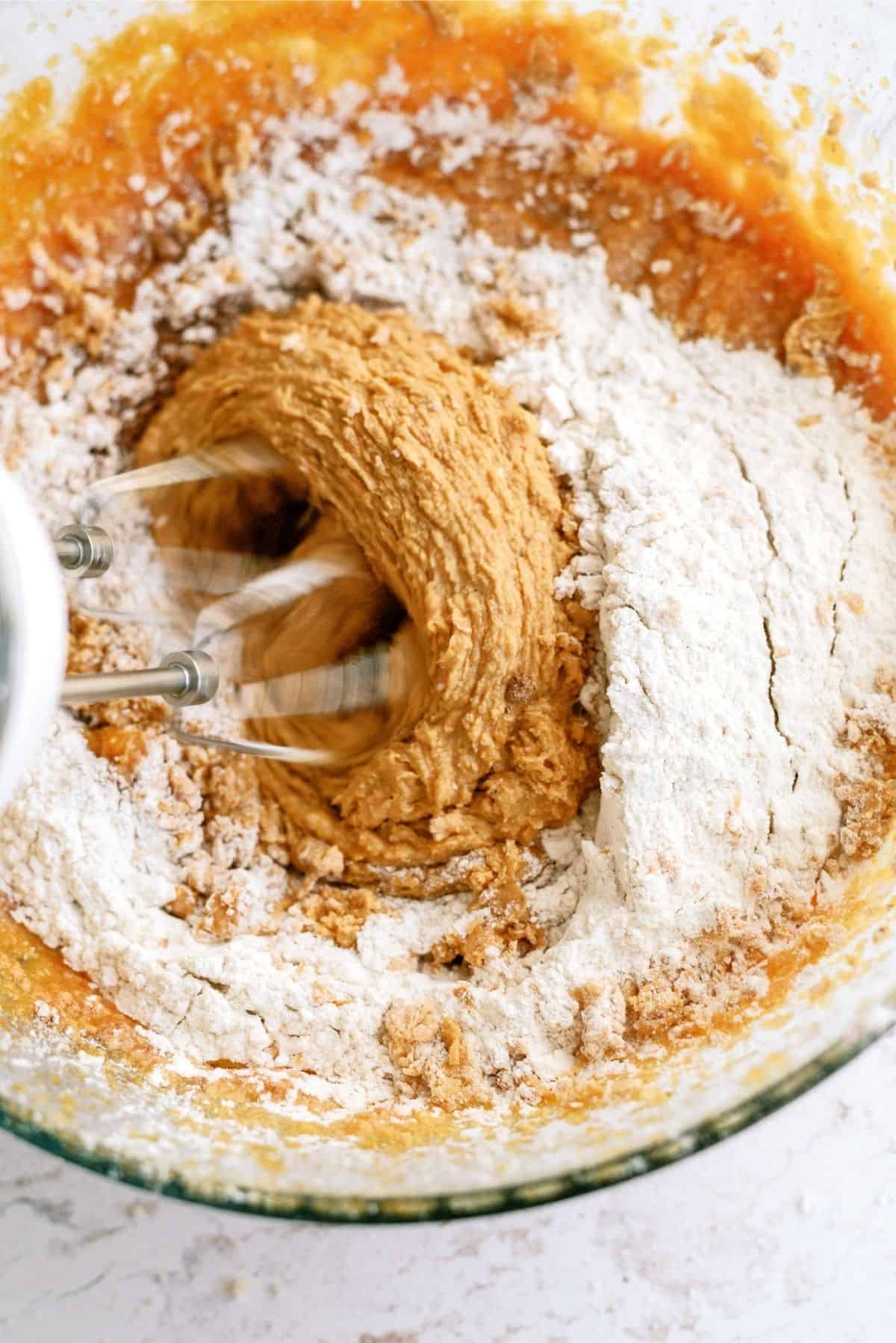 Dry ingredients added to wet ingredients and mixed with a hand mixer in a glass bowl