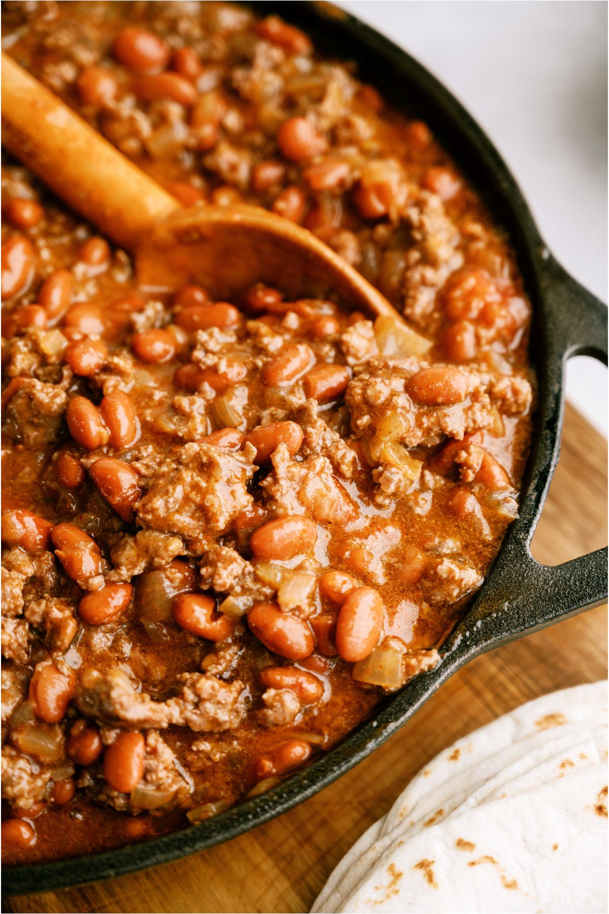 Ground beef and bean mixture for enchiladas in a skillet with a wooden spoon.