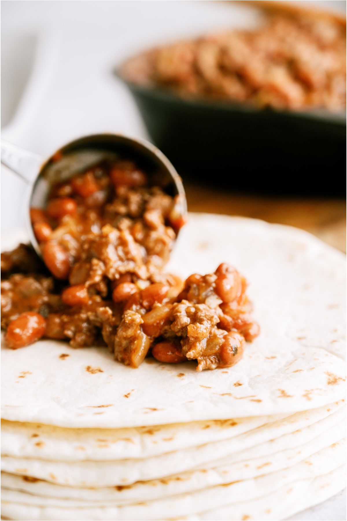 Scooping mixture onto a flour tortilla with the remaining mixture in the skillet in the background.