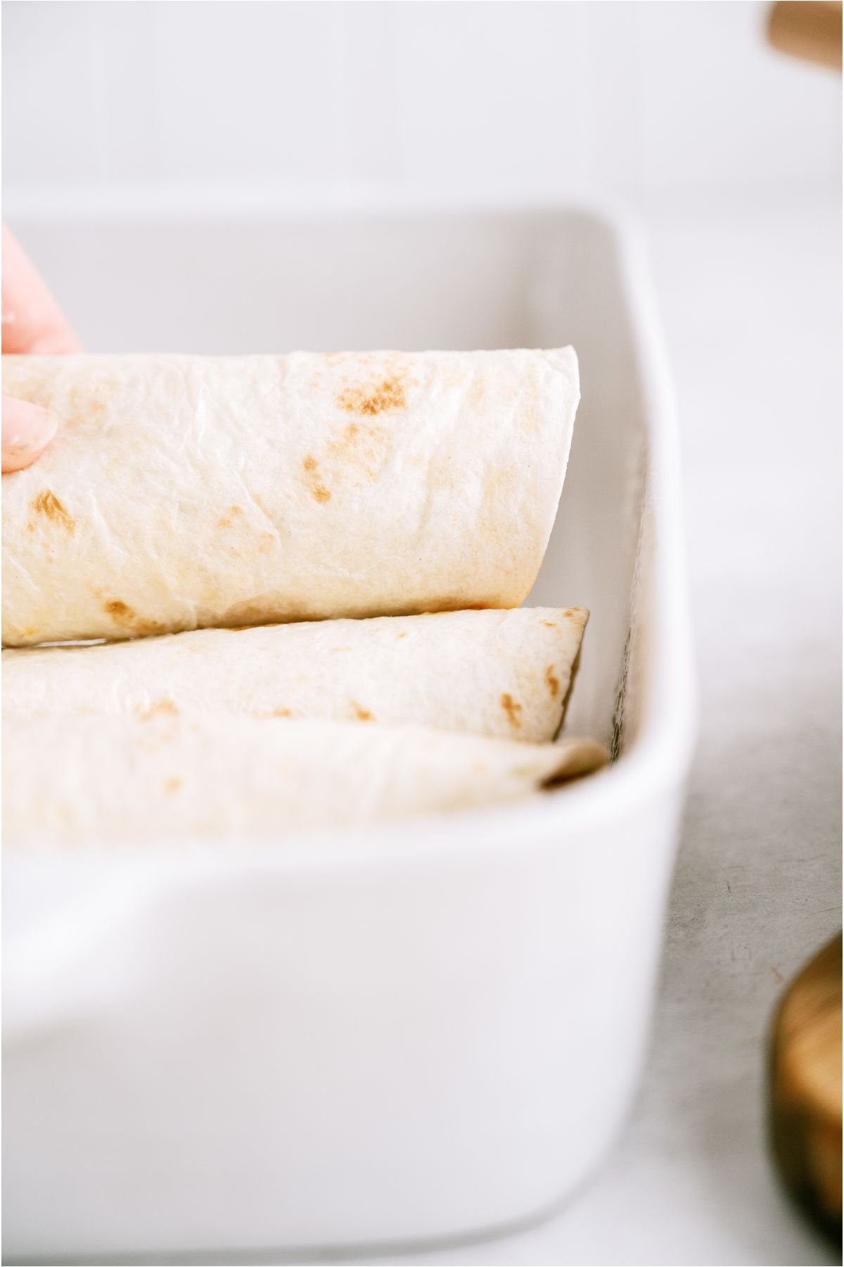 Rolled enchiladas being placed in a baking dish.
