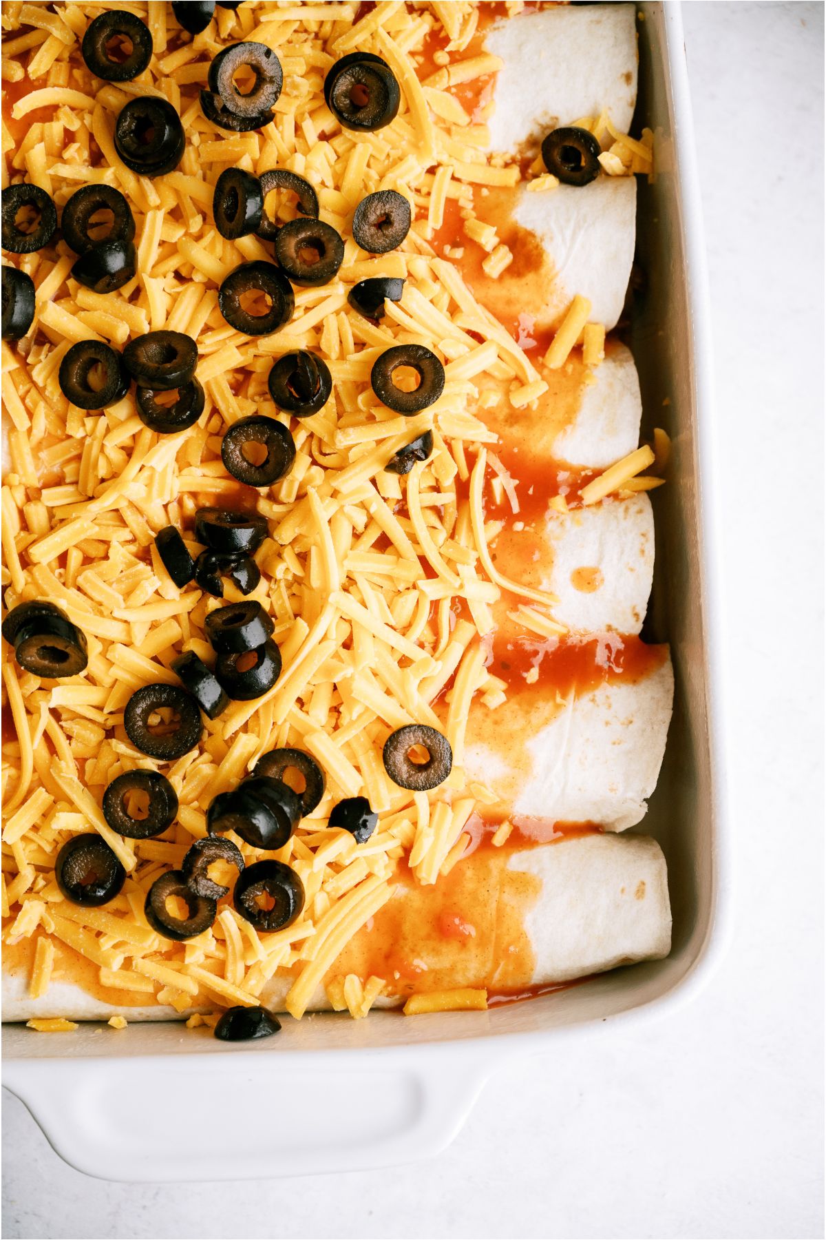 Enchiladas in baking dish topped with shredded cheese and sliced olives.