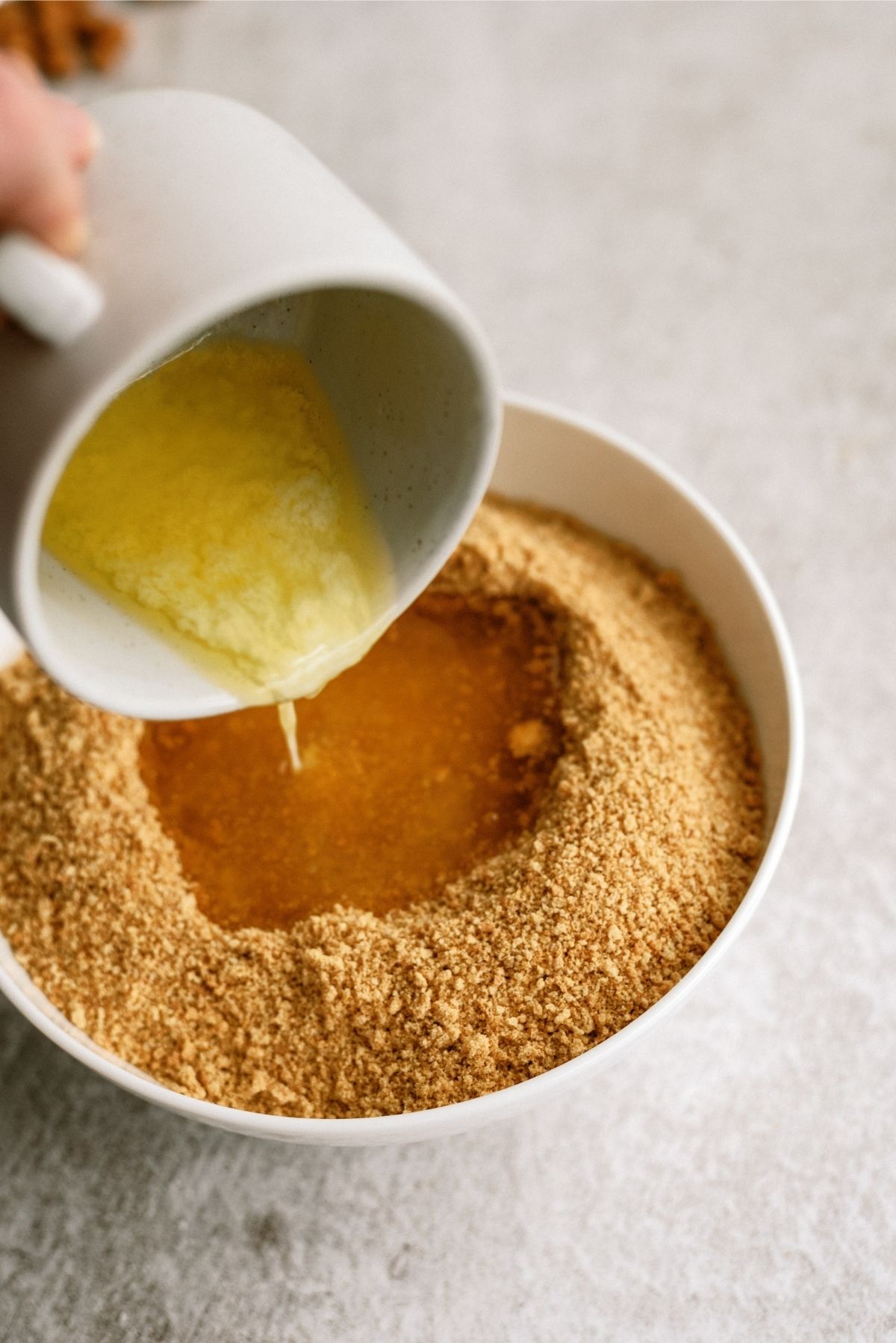 Pouring melted butter into a bowl of graham cracker crumbs