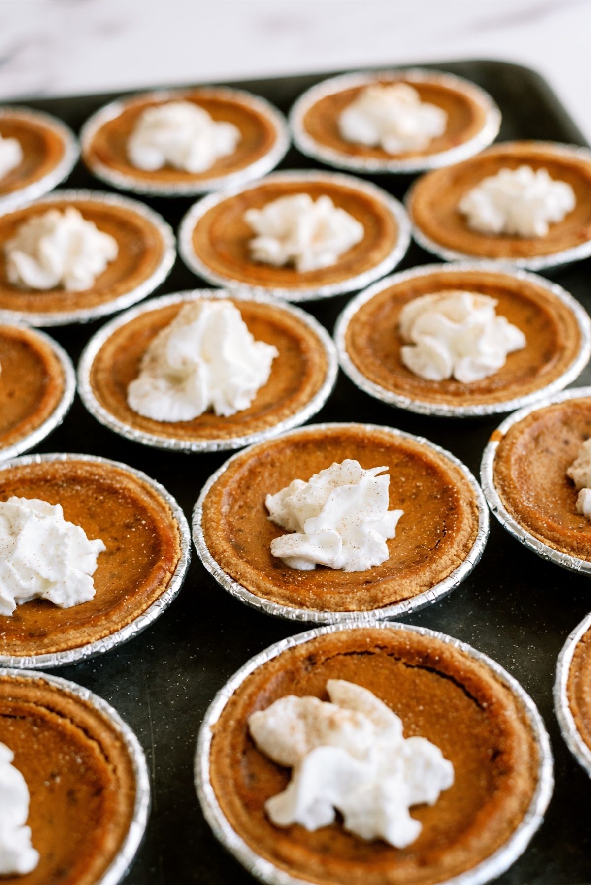 Mini Pumpkin Pies with Graham Cracker Crust on a sheet pan topped with whop cream