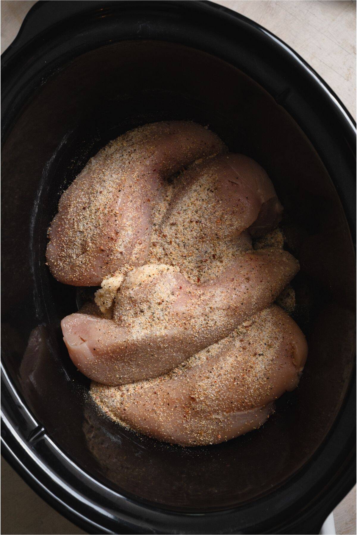 Chicken breasts, seasoned in the bottom of a slow cooker.