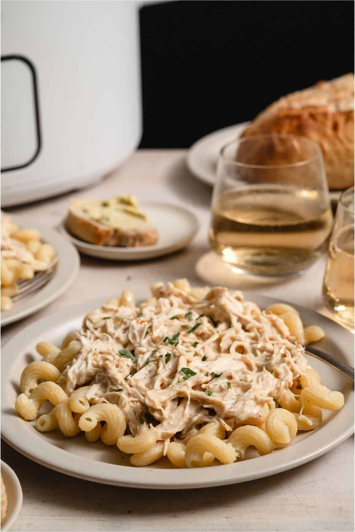 Slow Cooker Italian Chicken on a plate served over noodles with a slow cooker in the background.
