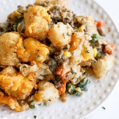 A serving of tater tot casserole with ground meat, mixed vegetables, and melted cheese on a white plate.
