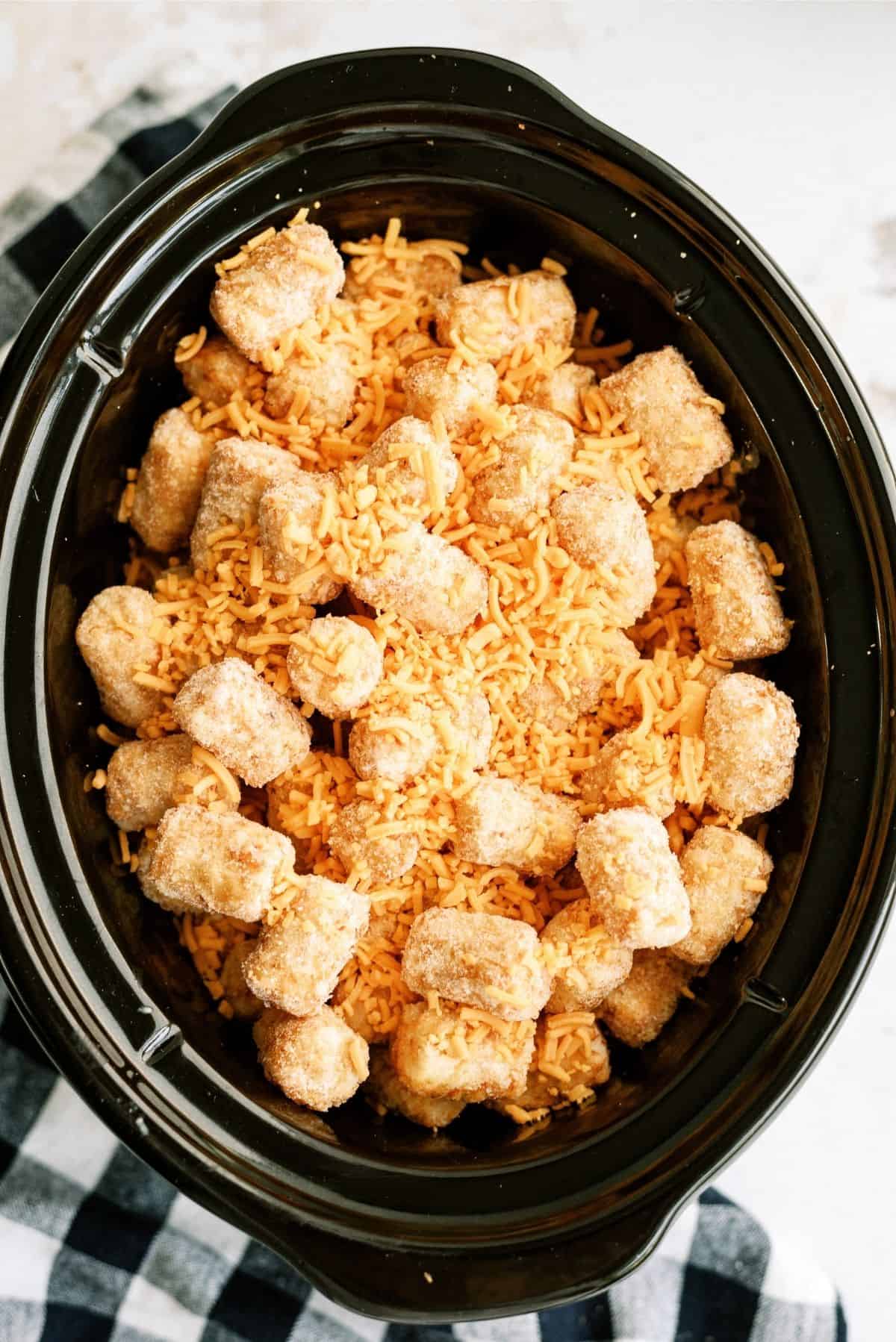 Uncooked Slow Cooker Tater Tot Cowboy Casserole topped with cheese in the slow cooker