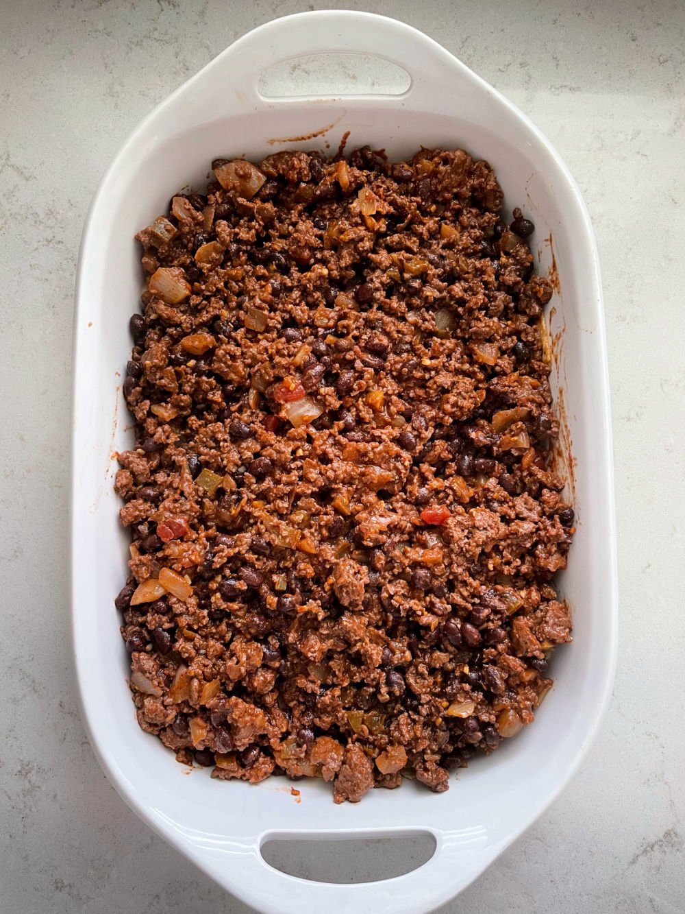 ground beef and bean mixture spread on top of crushed chips