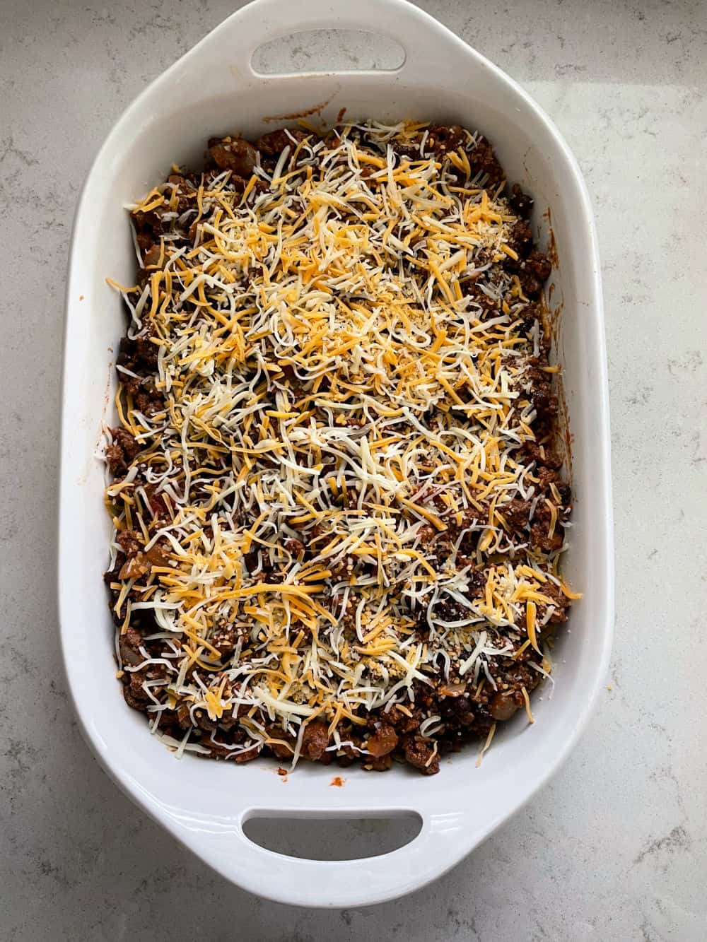 Shredded cheese on ground beef and bean mixture spread on top of crushed chips