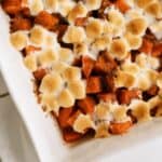 A baked yam casserole topped with toasted mini marshmallows in a white dish.