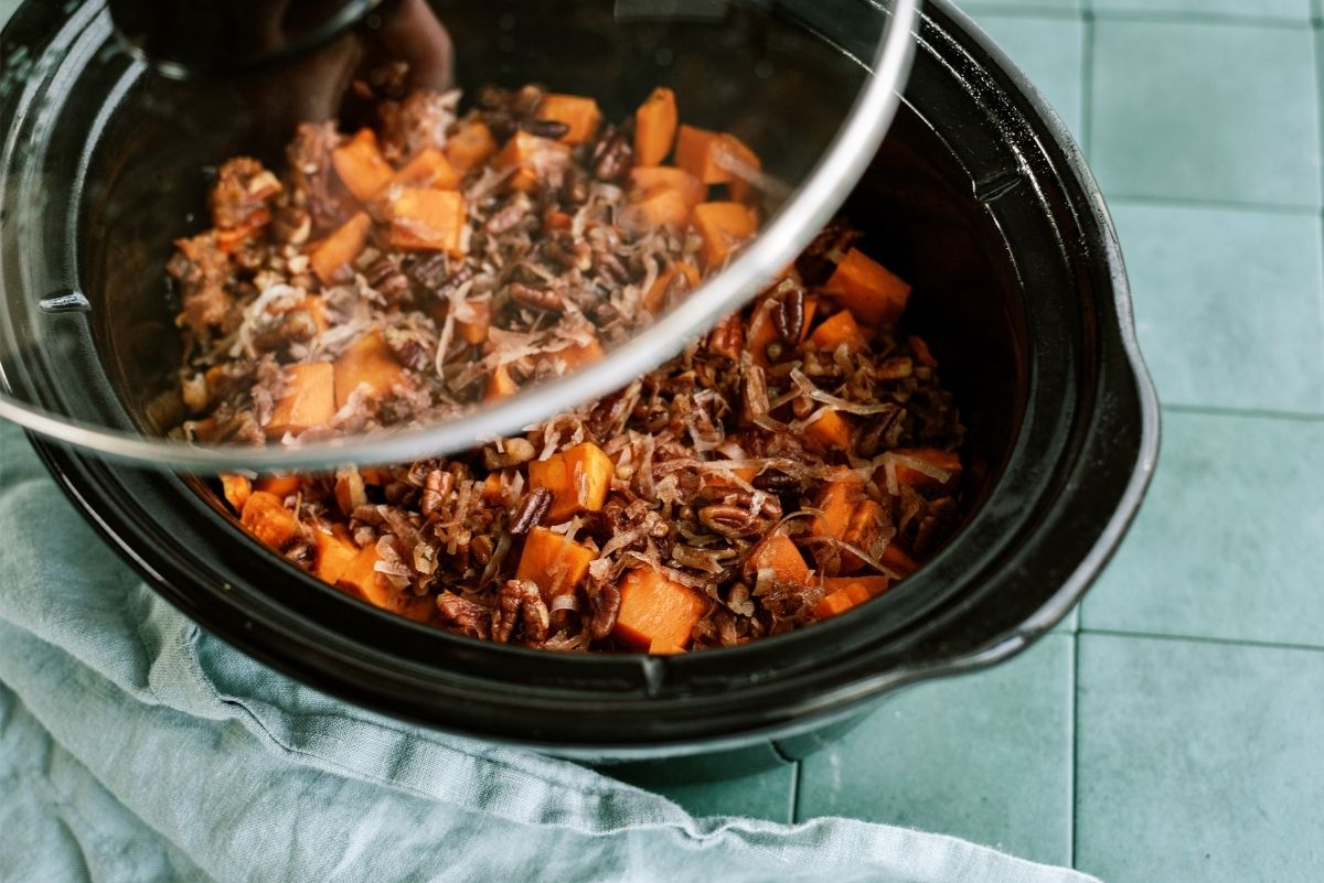 Placing lid on slow cooker filled with Coconut Pecan Sweet Potatoes