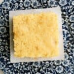 A square piece of cornbread sits on a white paper atop a blue and white floral-patterned plate.